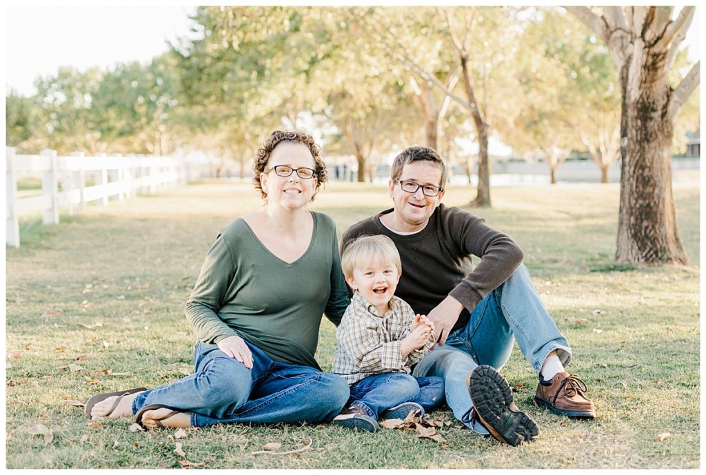 family photos at Morrison Ranch, family sitting on green grass, playing with fall leaves, under big green trees