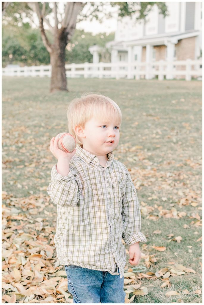 Little boy throwing baseball while standing in a pile of leaves in Morrison Ranch