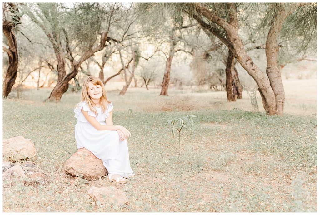 little girl in a white dress sitting on a rock in the middle of grass and trees at coons bluff