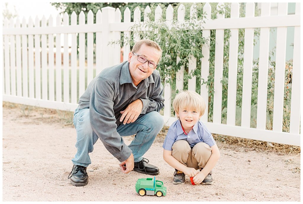 Dad and little boy playing with toy truck in front of white picket fence at Tumbleweed Park, Jette's Family Photos 