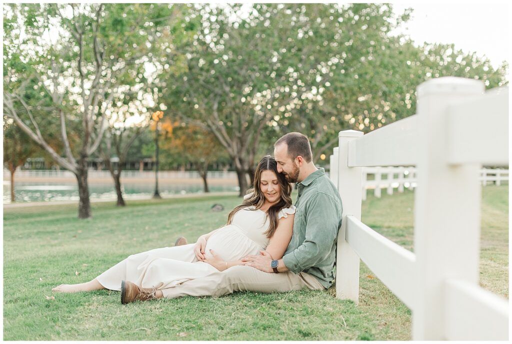 mom and dad leaning on white picket fence and snuggled up with baby bump