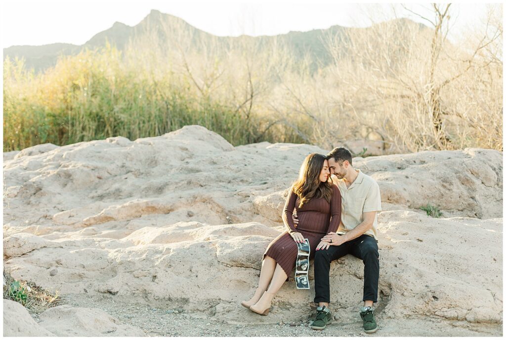 Phon D. Sutton Baby Announcement Photos | Couple with ultra sound sitting on rocks with beautiful mountain range in the back