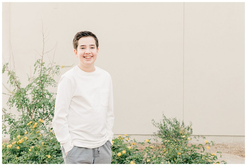 A boy standing in front of a cream wall wearing a white shirt in Downtown Gilbert