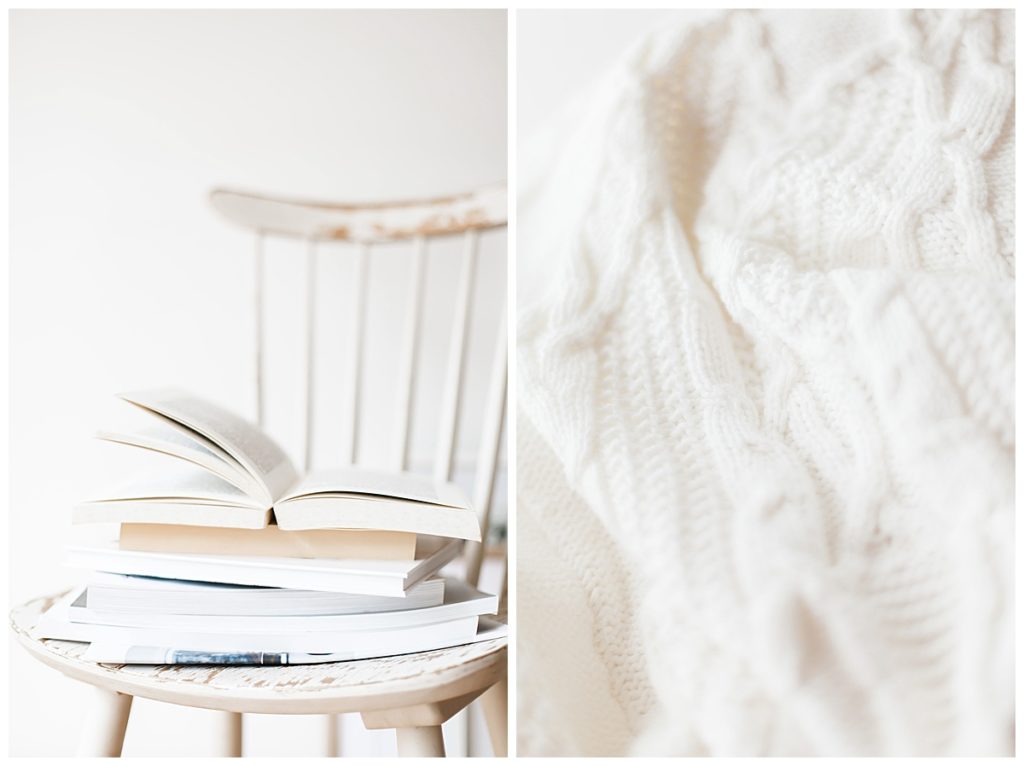 books stacked on a white chair nest to a cozy white blanket