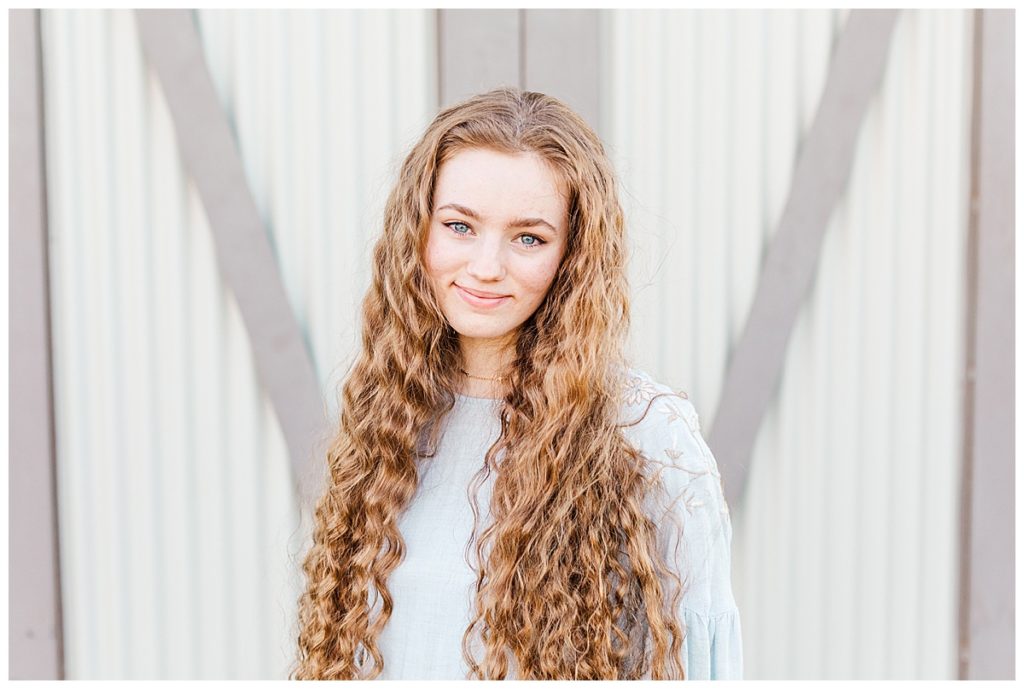 Addi's senior photos, standing in front of barn door at Layton Lakes smiling directly toward the camera 