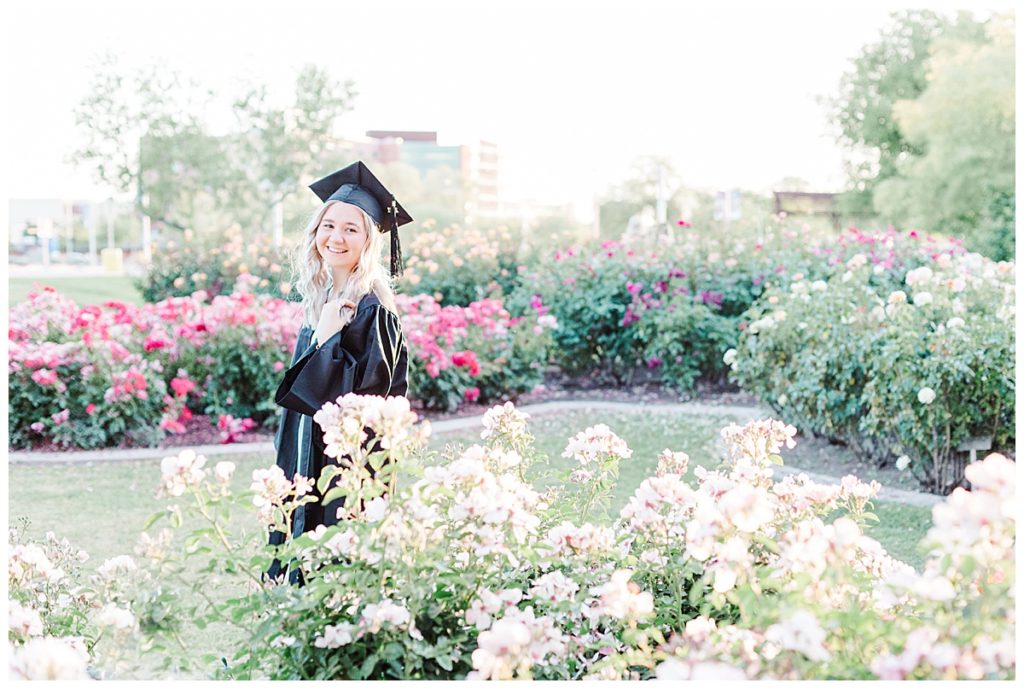 rose garden senior photos, girl wearing cap and gown standing in white flowers at the MCC rose garden