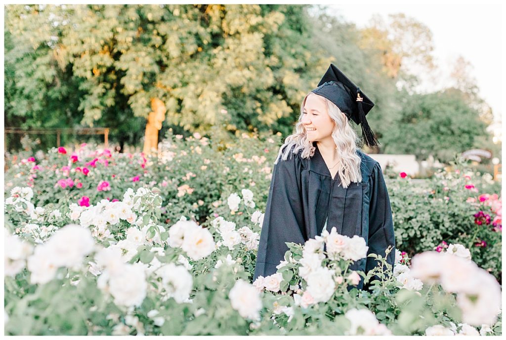 rose garden senior photos, girl wearing cap and gown standing in a field of white roses at MCC rose garden