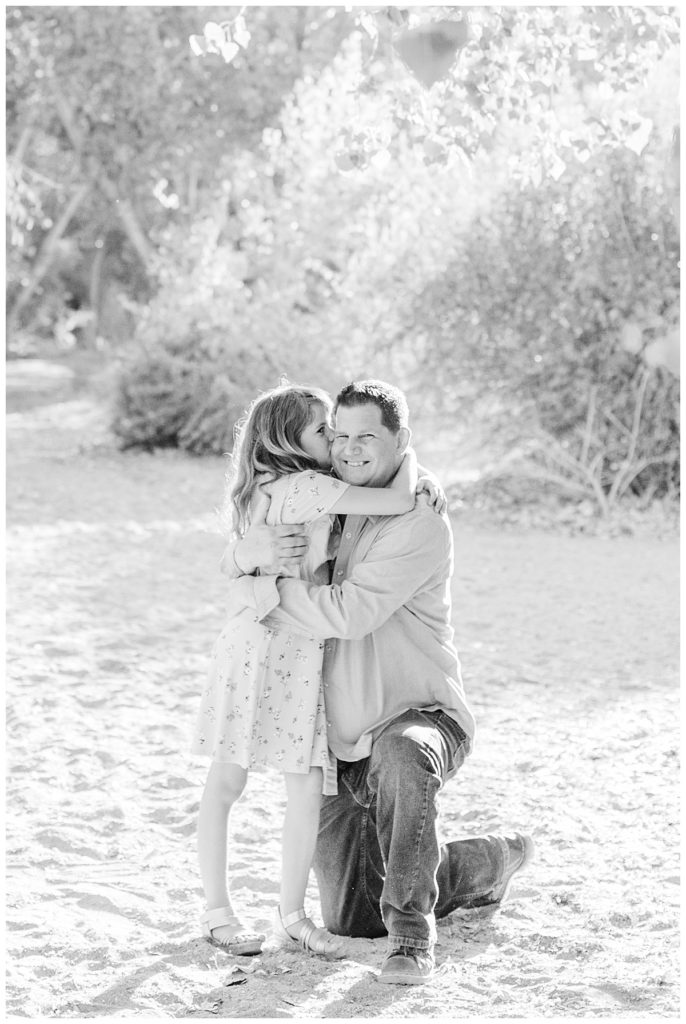 a black and white photo of a daughter kissing her dad, who is down on his knees