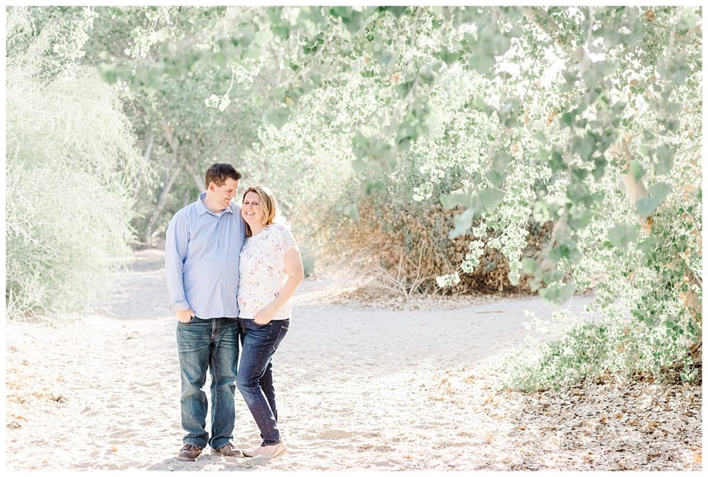 Ison's family photos, couple standing together laughing under big green trees at queen creek wash 