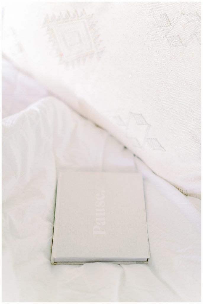 a white book titled, pause, on a white bed, The Ruthless Elimination of Hurry