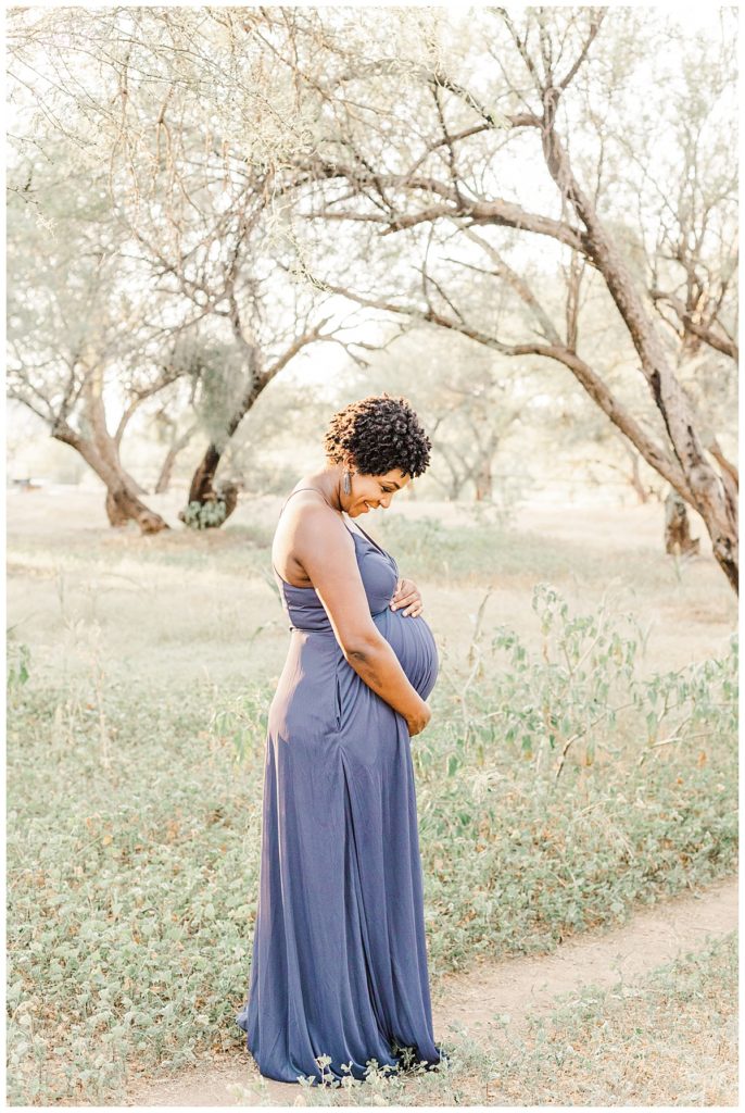 mom wearing a long purple dress smiling towards her baby bump, in a field at coons bluff