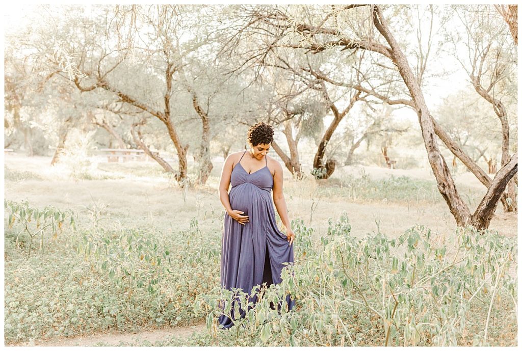 mom walking through a field in coons bluff wearing a long purple dress and holding her baby bump