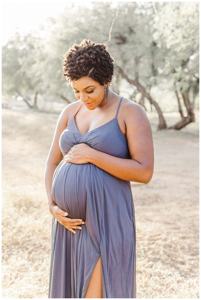 Abby’s Arizona Maternity Session, women wearing a long purple dress smiling toward her baby bump