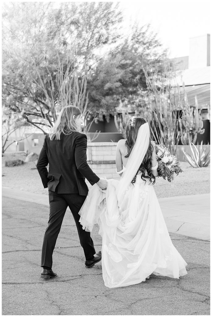 Black and white of bride and groom walking back to reception at Candice & Joel's Private Estate Scottsdale Wedding 